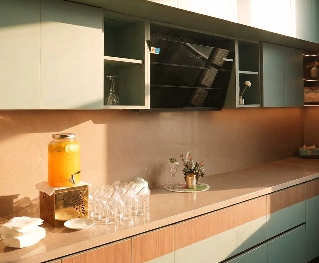 Mint green kitchen with lift-up cabinets and warm stone backsplash in sunlight